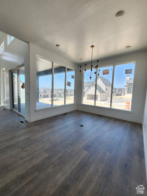 Unfurnished dining area featuring dark wood-style flooring, a chandelier, plenty of natural light, and a textured ceiling
