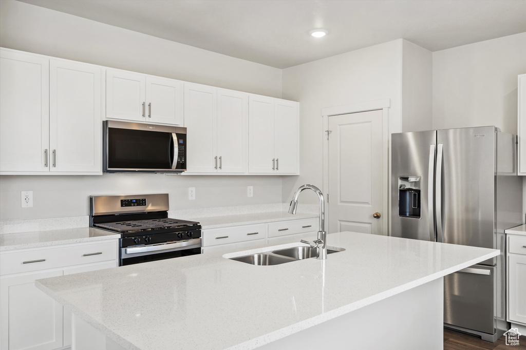Kitchen featuring appliances with stainless steel finishes, a center island with sink, white cabinetry, light stone countertops, and recessed lighting