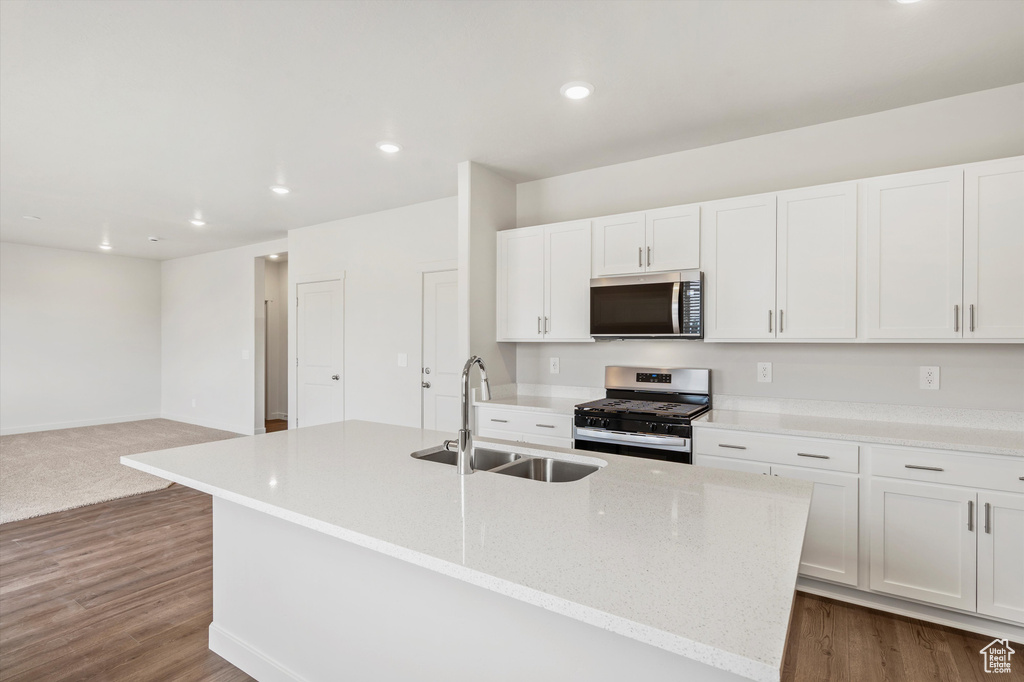 Kitchen with stainless steel appliances, white cabinetry, an island with sink, recessed lighting, and light stone countertops