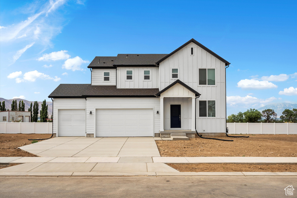 Modern farmhouse style home featuring an attached garage, driveway, roof with shingles, board and batten siding, and a mountain view