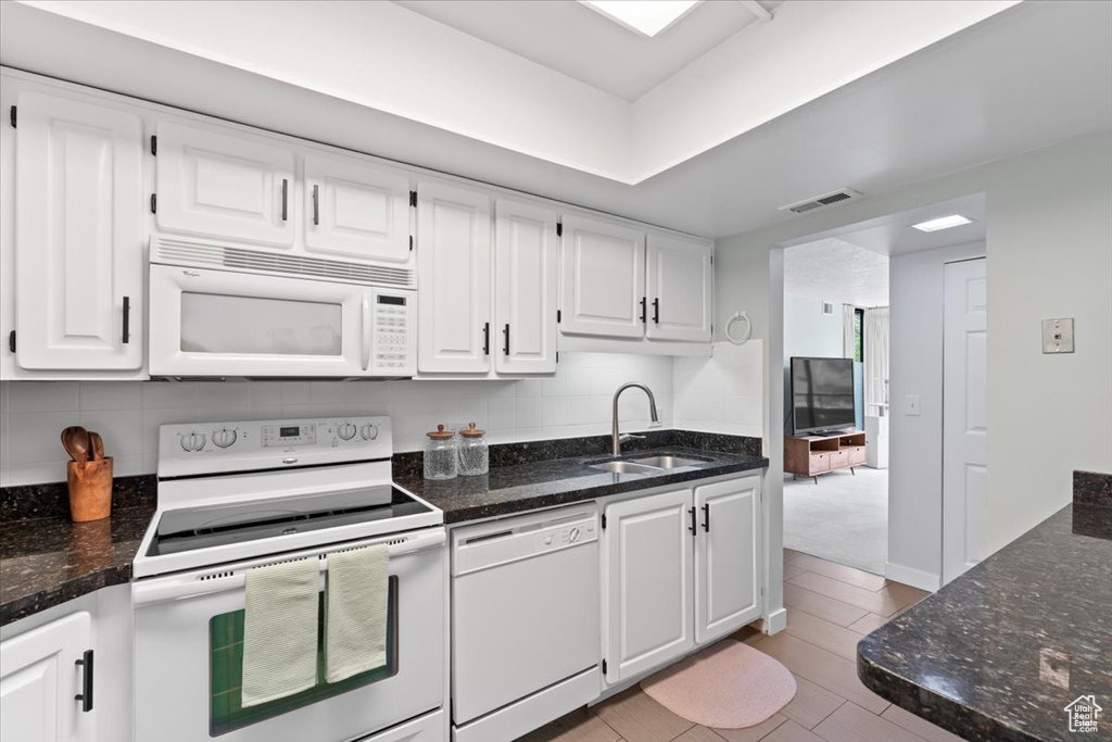 Kitchen with white cabinetry, dark stone counters, a sink, and white appliances