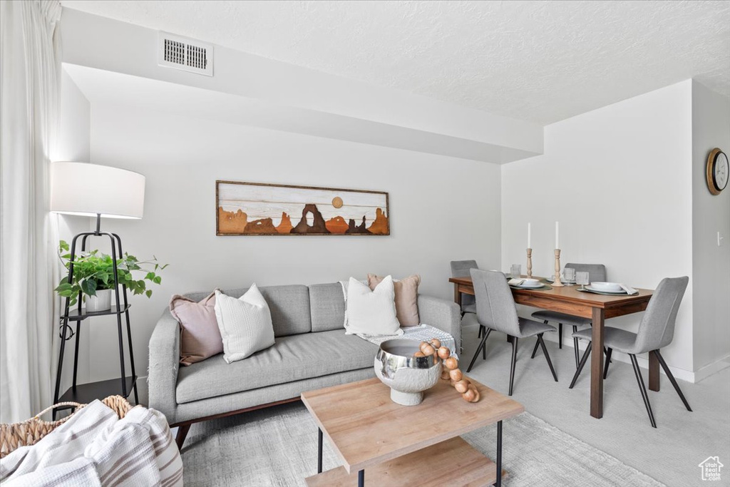 Living area featuring light colored carpet, a textured ceiling, and visible vents