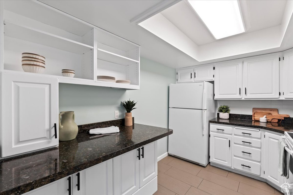 Kitchen featuring open shelves, freestanding refrigerator, white cabinets, and dark stone countertops