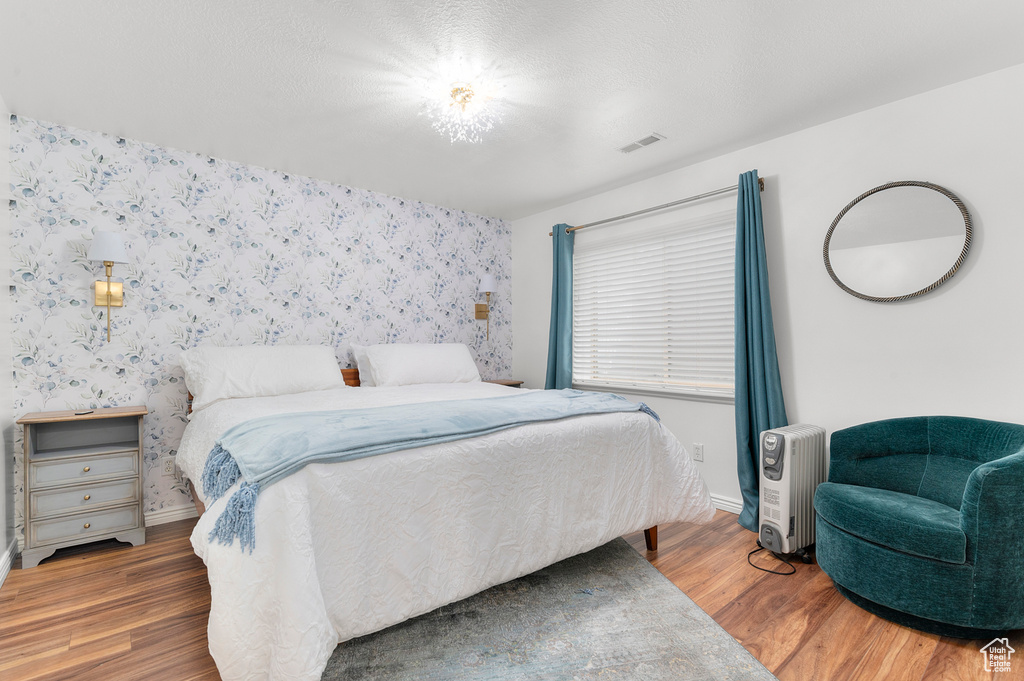 Bedroom featuring wallpapered walls, wood finished floors, visible vents, and baseboards