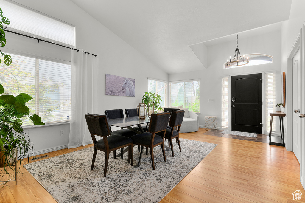 Dining space featuring visible vents, light wood-type flooring, baseboards, a chandelier, and high vaulted ceiling