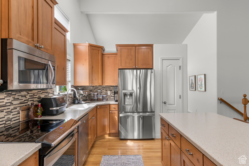Kitchen featuring a sink, brown cabinetry, decorative backsplash, light wood-style floors, and stainless steel appliances