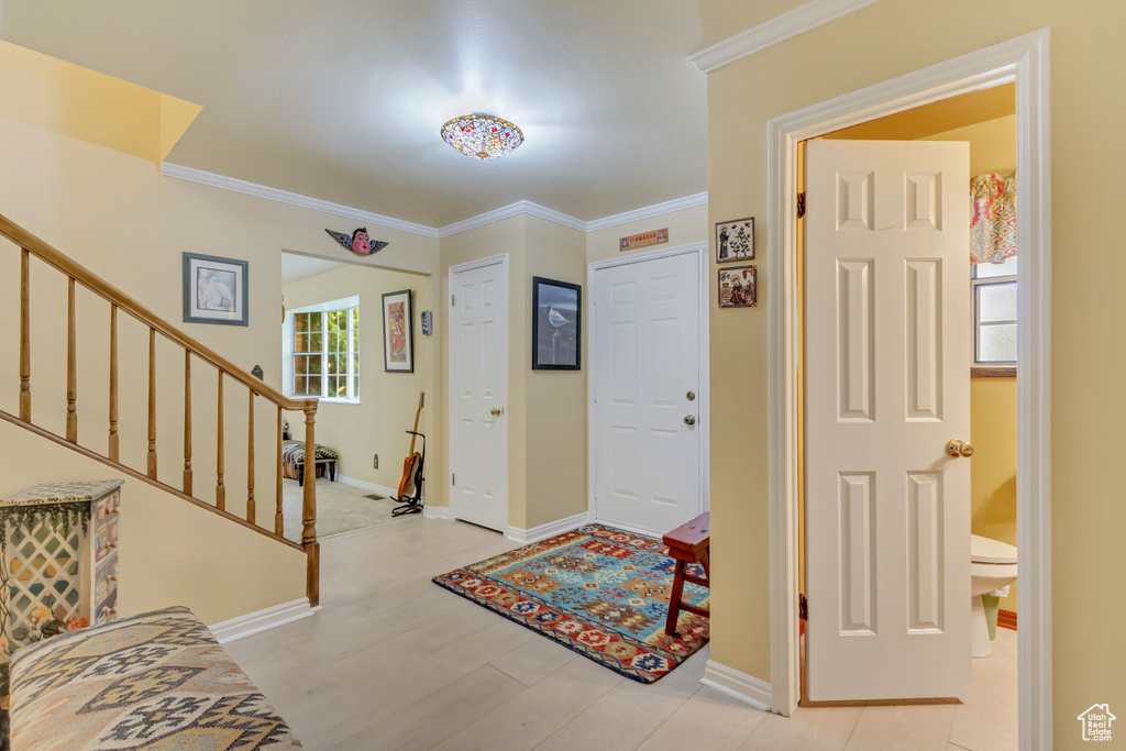 Foyer entrance featuring stairway, baseboards, ornamental molding, and light wood finished floors