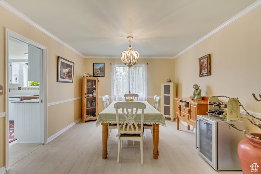 Dining space with baseboards, crown molding, a chandelier, and light wood-style flooring