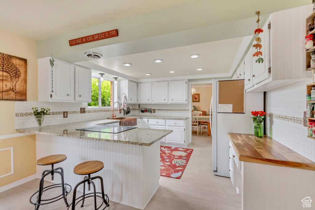 Kitchen featuring a peninsula, electric cooktop, white cabinetry, decorative backsplash, and light stone counters