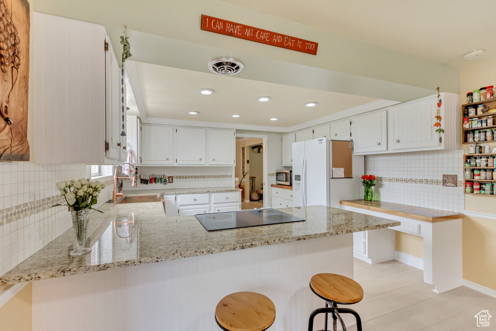 Kitchen featuring a peninsula, stainless steel microwave, backsplash, white refrigerator with ice dispenser, and cooktop