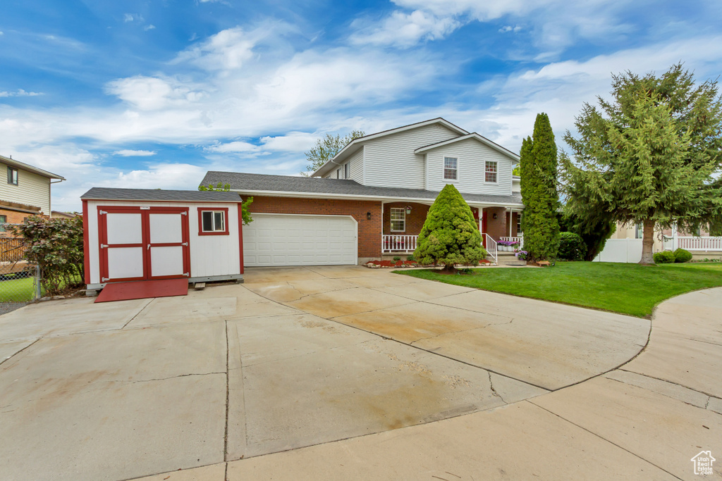 Traditional-style home featuring a storage shed, an attached garage, fence, a porch, and a front yard