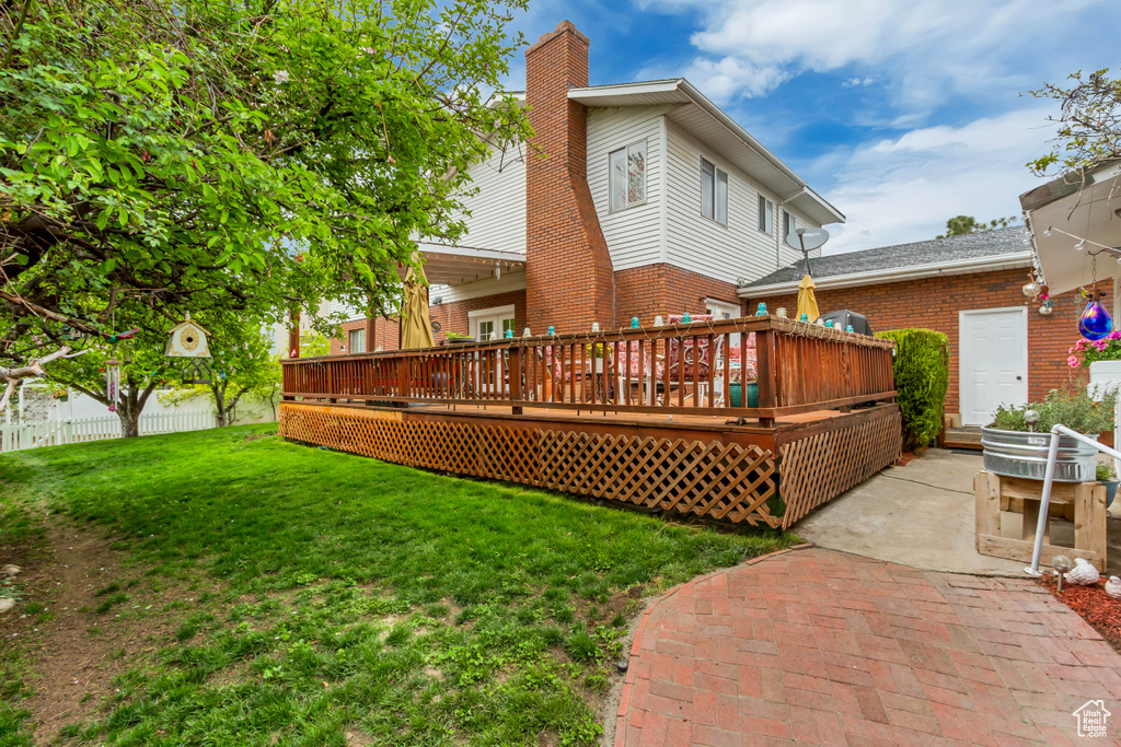 Rear view of property with brick siding, a yard, a wooden deck, and a chimney