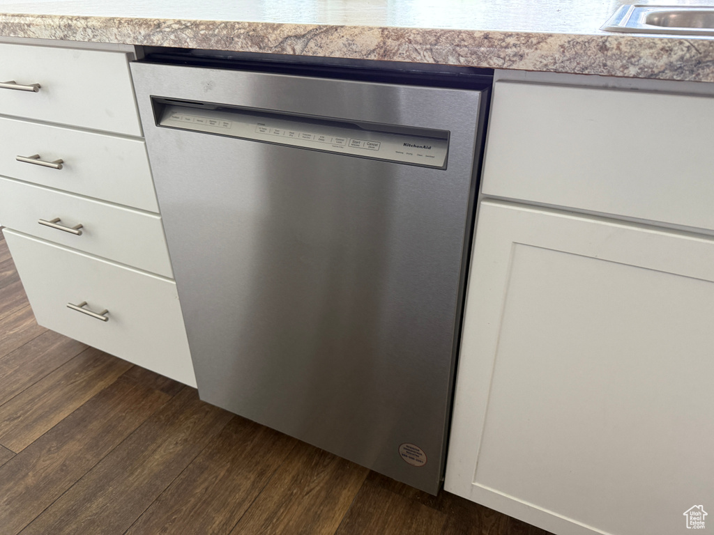 Kitchen view of dishwasher, dark wood-type flooring, white cabinetry, and light countertops