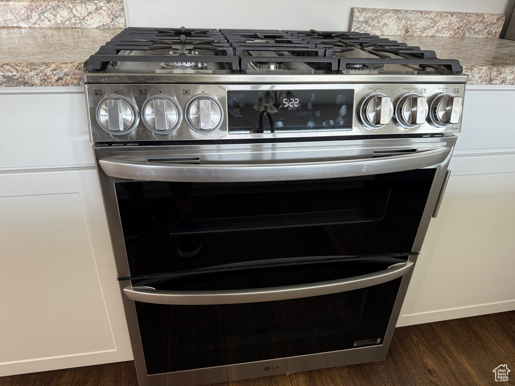 Detailed view of double oven range, dark wood finished floors, light countertops, and white cabinetry
