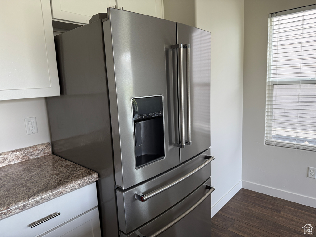 Kitchen with stainless steel refrigerator with ice dispenser, dark wood finished floors, and white cabinets