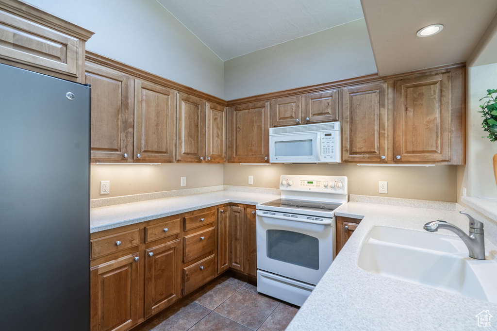 Kitchen with white appliances, a sink, light countertops, dark tile patterned flooring, and brown cabinetry