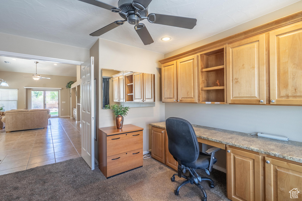 Home office featuring ceiling fan, built in desk, tile patterned flooring, baseboards, and carpet floors