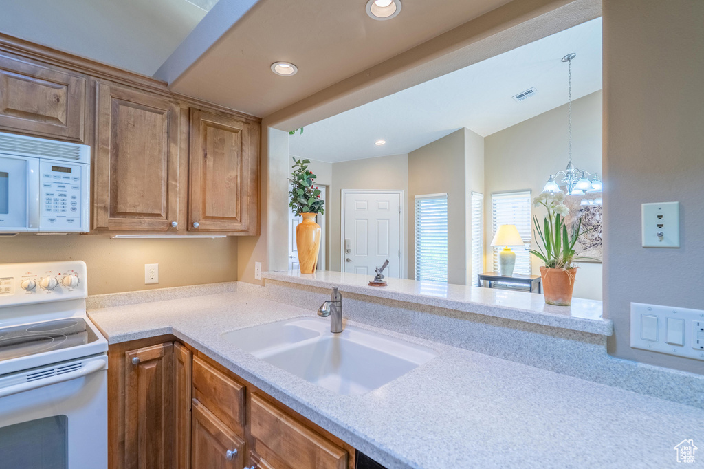 Kitchen featuring white appliances, a sink, light countertops, recessed lighting, and brown cabinetry
