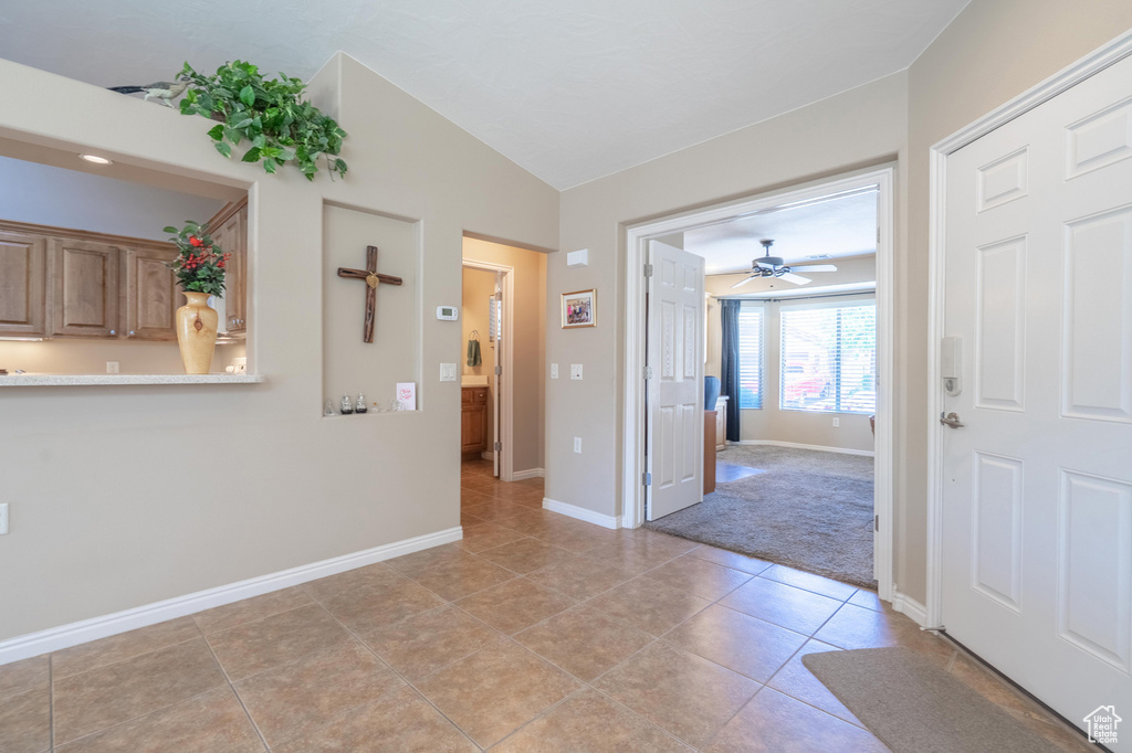 Spare room with baseboards, vaulted ceiling, light tile patterned floors, a ceiling fan, and light colored carpet