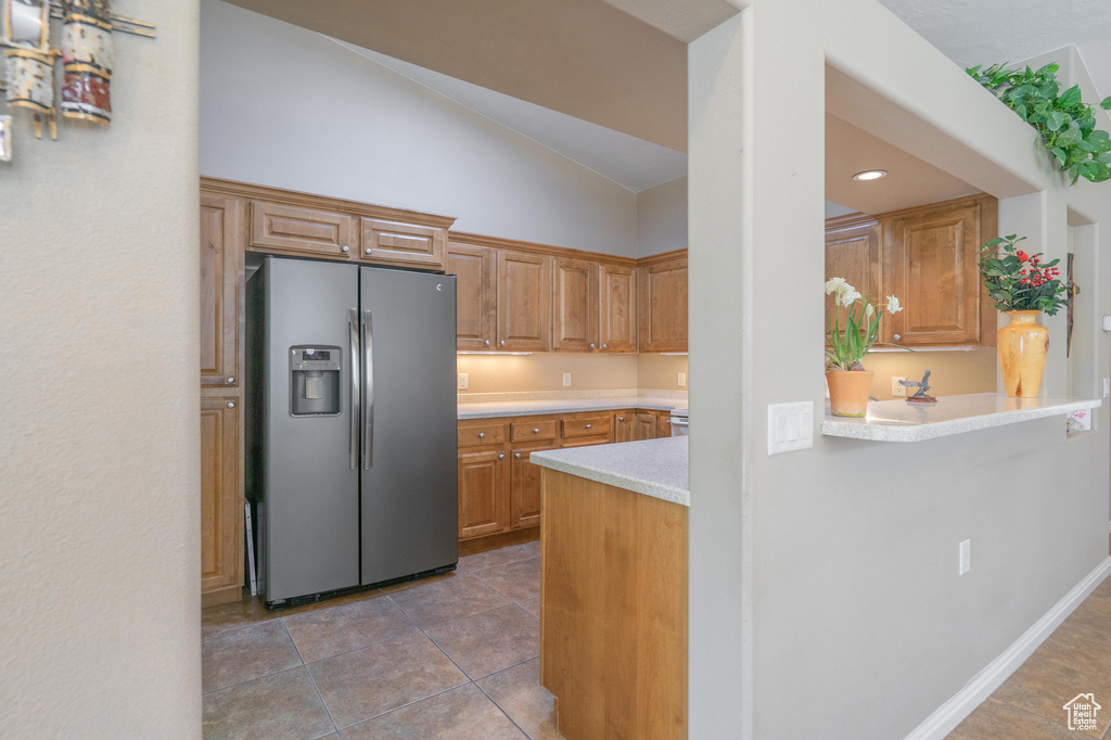 Kitchen featuring stainless steel fridge, vaulted ceiling, light countertops, light tile patterned flooring, and recessed lighting