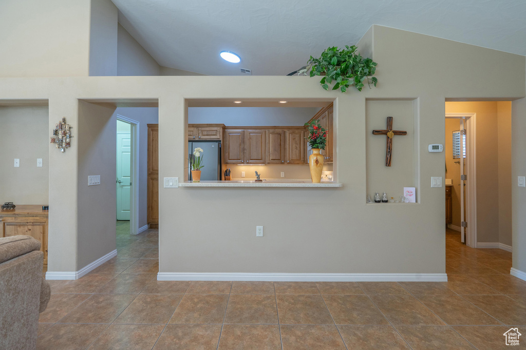 Kitchen with freestanding refrigerator, vaulted ceiling, baseboards, light countertops, and brown cabinets