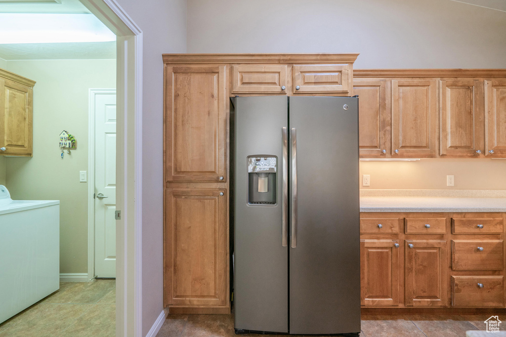 Kitchen with stainless steel refrigerator with ice dispenser, washer / dryer, light countertops, and baseboards