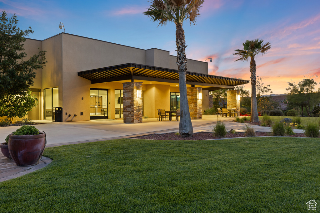 Rear view of property featuring stucco siding, a lawn, stone siding, and a patio