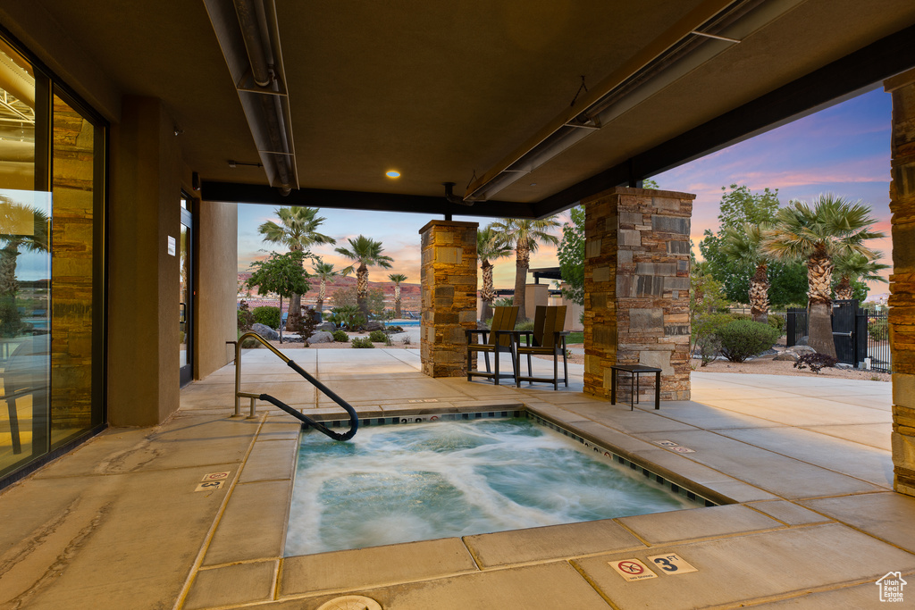 Pool at dusk featuring a hot tub and a patio