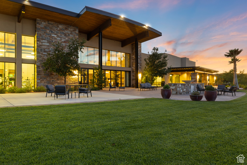 Rear view of property featuring a patio area, stone siding, and a lawn