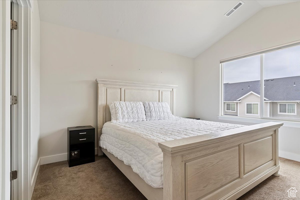 Bedroom with lofted ceiling, visible vents, baseboards, and light carpet