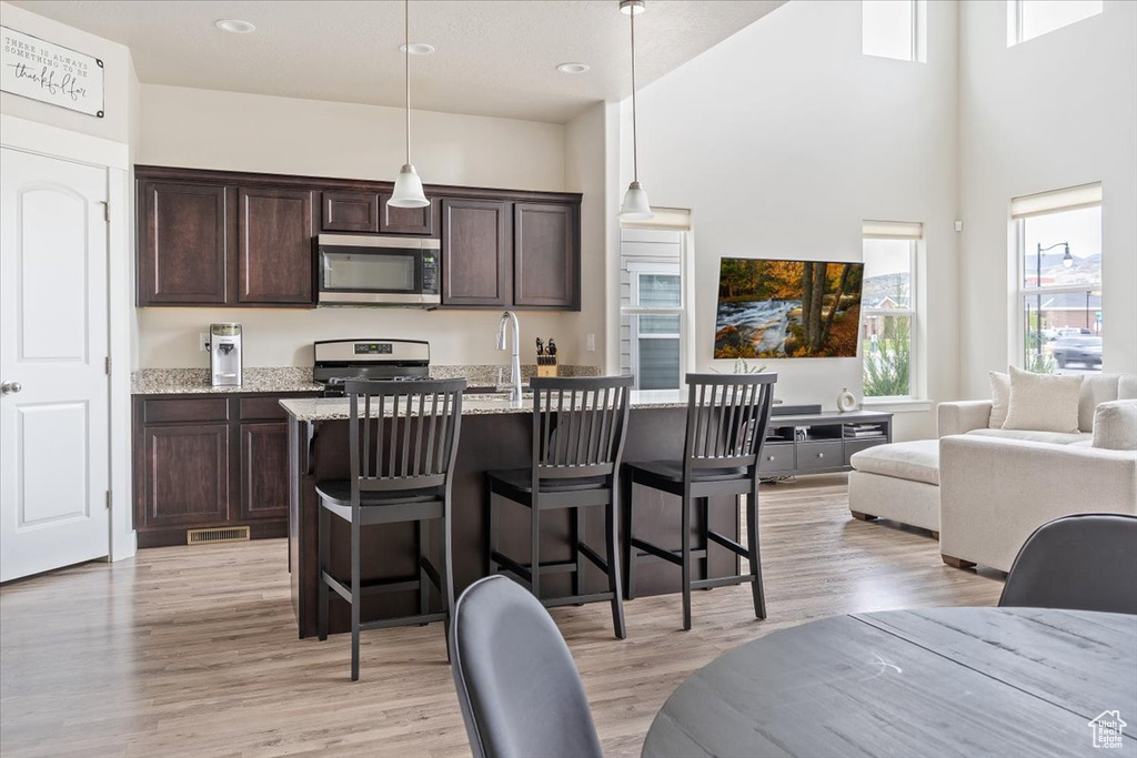 Kitchen with appliances with stainless steel finishes, a towering ceiling, a breakfast bar area, and dark brown cabinetry