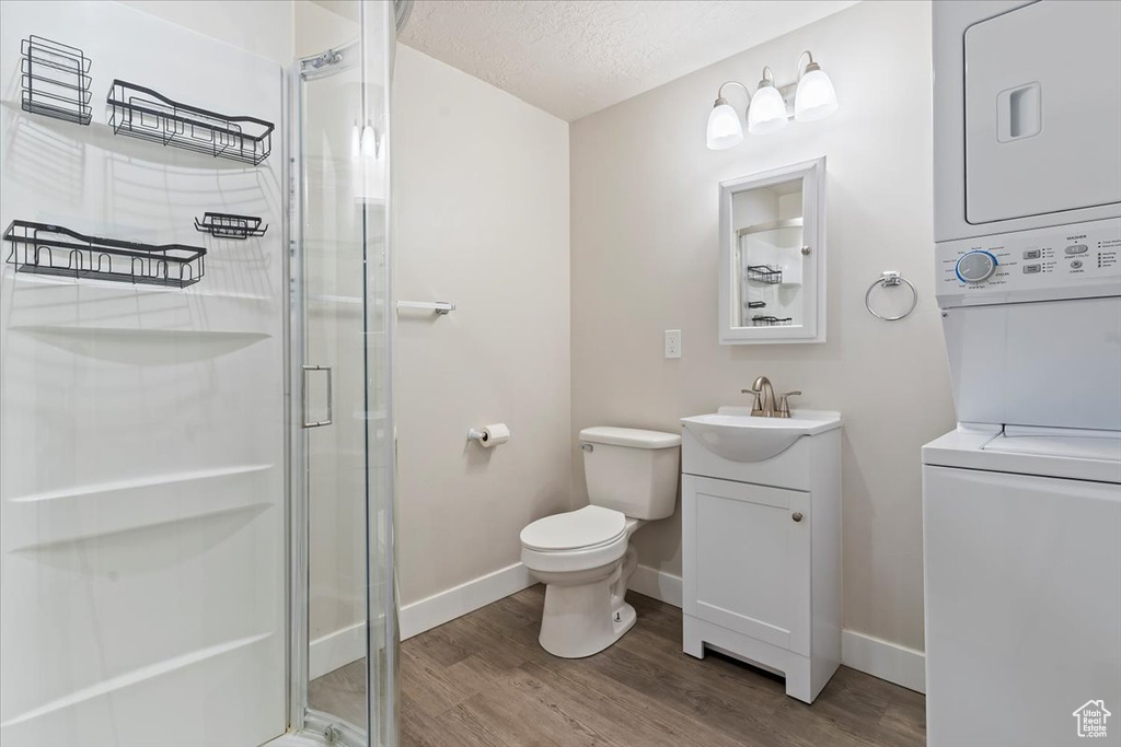 Full bath featuring stacked washer and dryer, toilet, a stall shower, baseboards, and wood finished floors