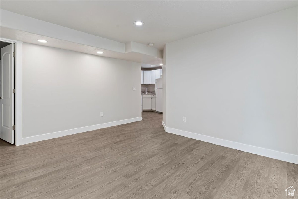 Basement with light wood-type flooring, baseboards, freestanding refrigerator, and recessed lighting