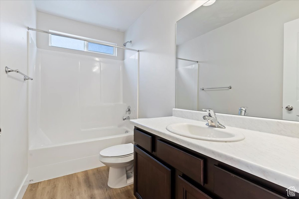Bathroom featuring wood finished floors, tub / shower combination, vanity, and toilet