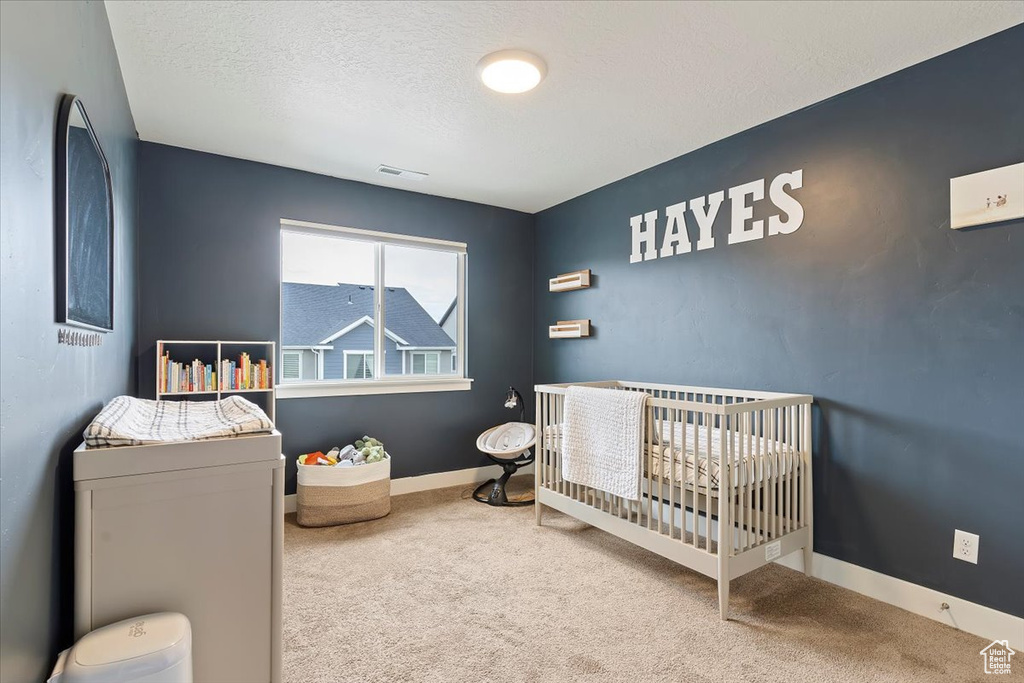 Bedroom featuring a nursery area, baseboards, carpet flooring, and a textured ceiling