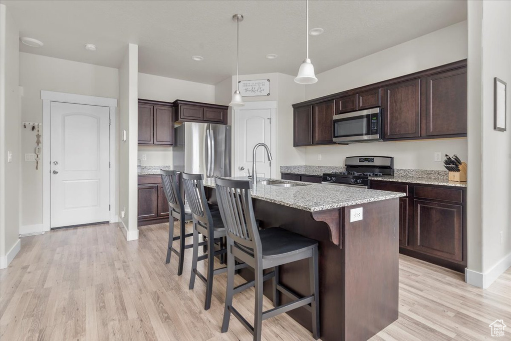 Kitchen with dark brown cabinets, a sink, a breakfast bar, stainless steel appliances, and light wood-style flooring