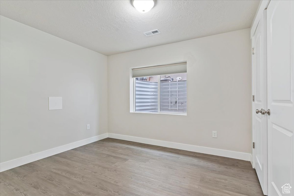 Empty room with a textured ceiling, visible vents, light wood finished floors, and baseboards