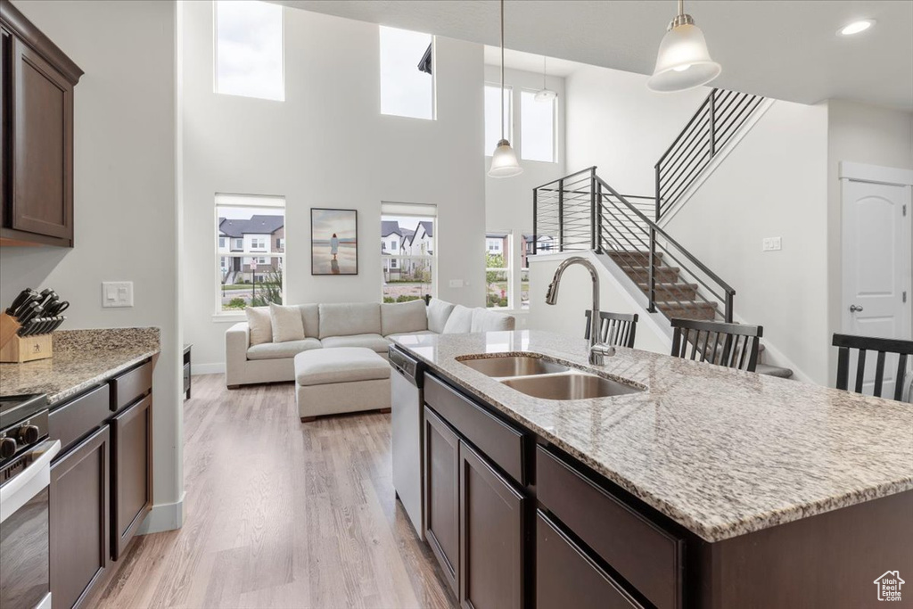Kitchen featuring dark brown cabinets, a sink, an island with sink, pendant lighting, and light wood finished floors