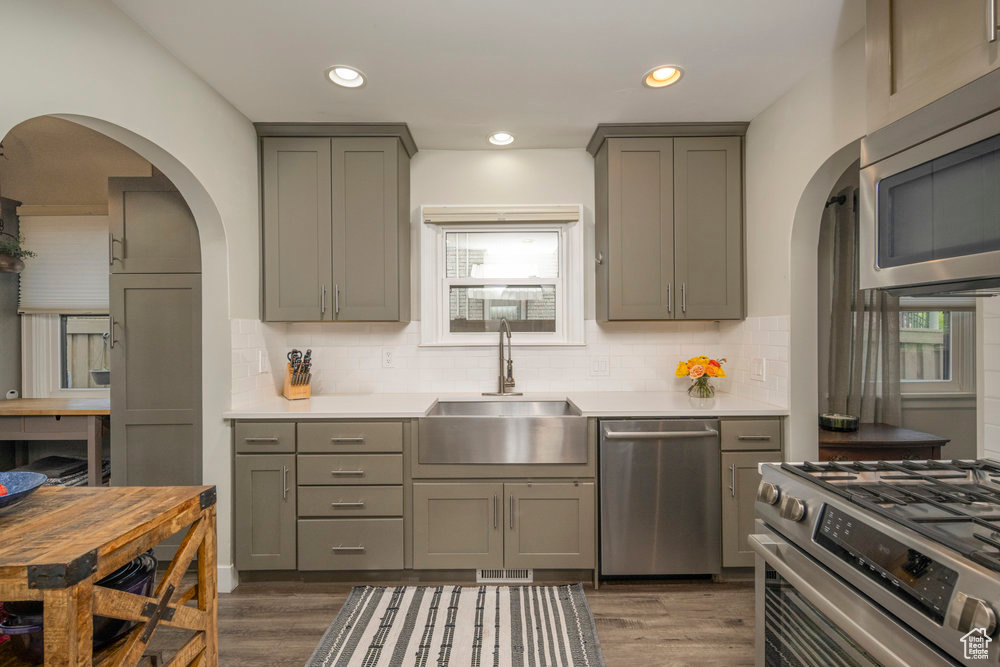 Kitchen featuring arched walkways, a sink, appliances with stainless steel finishes, and gray cabinets