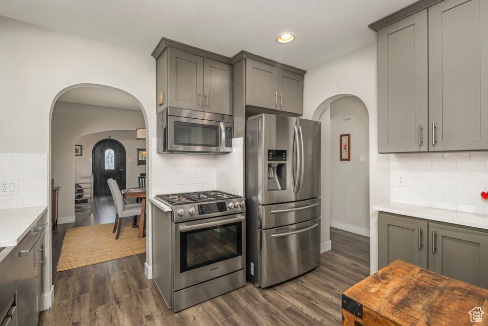 Kitchen with arched walkways, light countertops, appliances with stainless steel finishes, and decorative backsplash