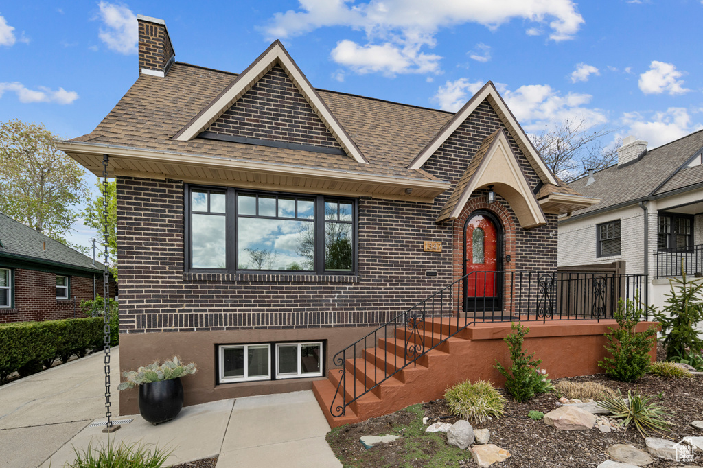 Tudor-style house featuring a shingled roof, brick siding, and a patio