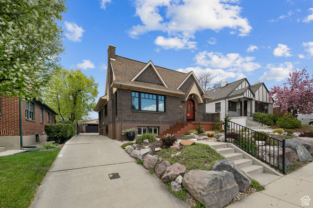 Tudor-style house featuring a shingled roof, a chimney, brick siding, and a garage
