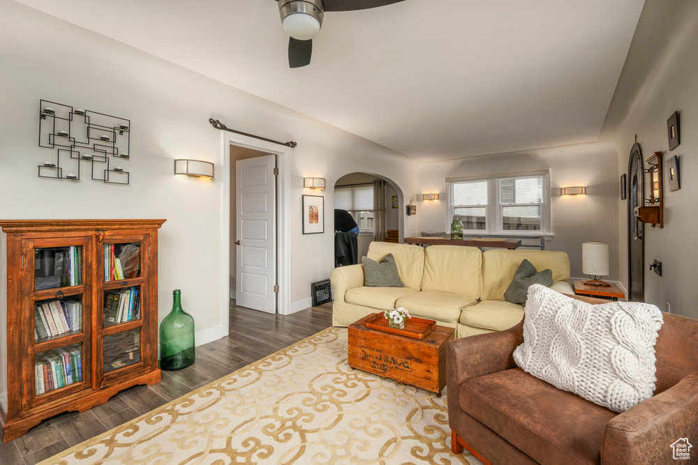Living room with arched walkways, dark wood finished floors, baseboards, and ceiling fan