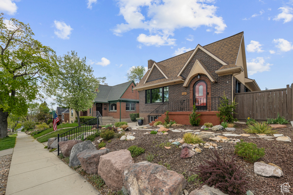 English style home with brick siding, roof with shingles, fence, and a chimney