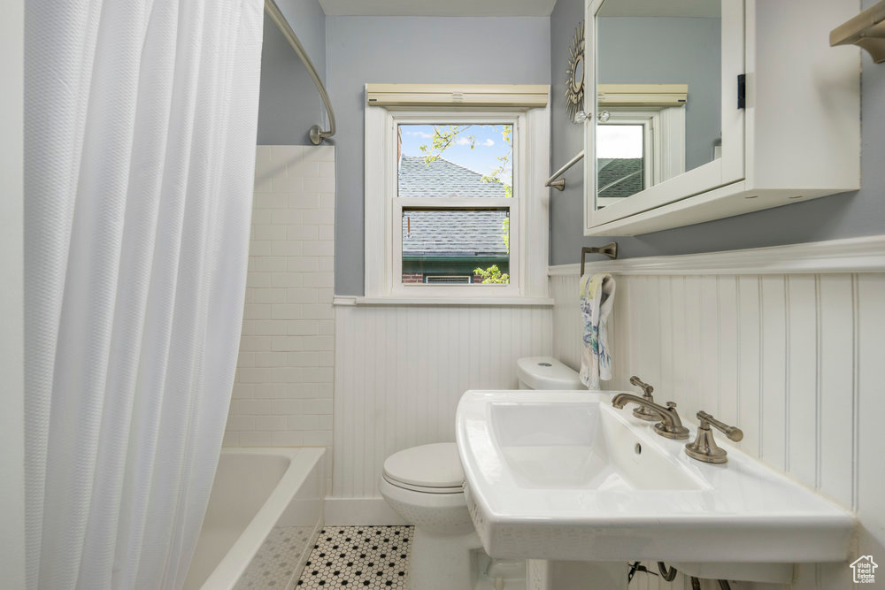 Bathroom with tile patterned floors, a wainscoted wall, toilet, a sink, and shower / tub combo