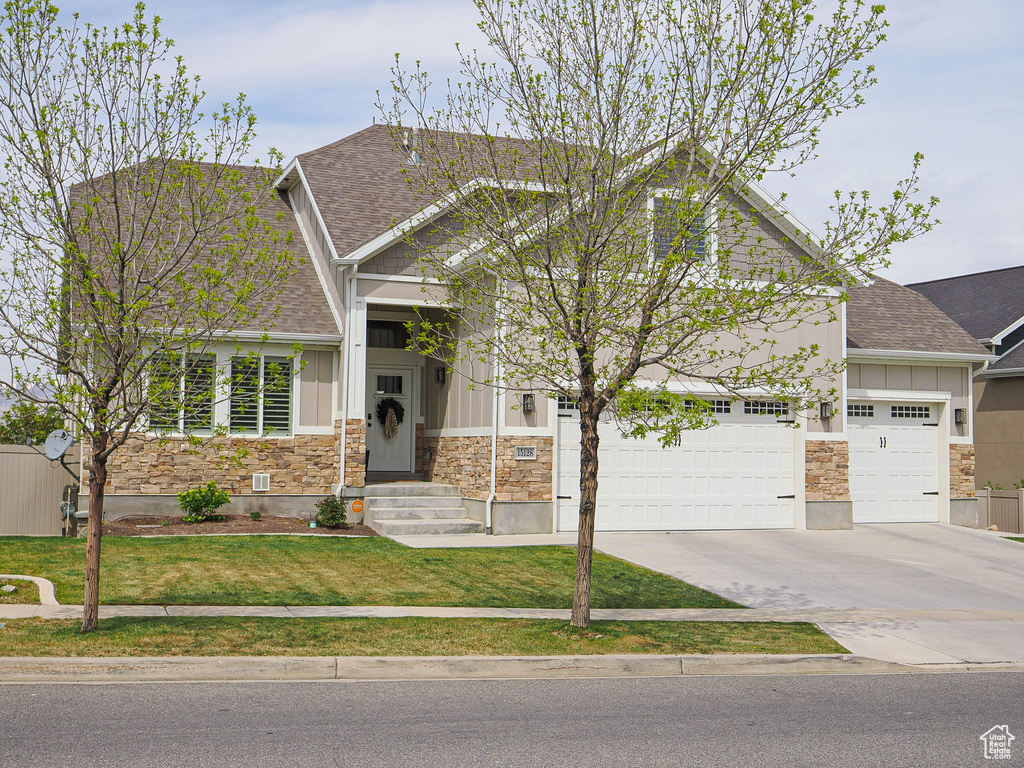 Craftsman inspired home featuring roof with shingles, stone siding, board and batten siding, and driveway