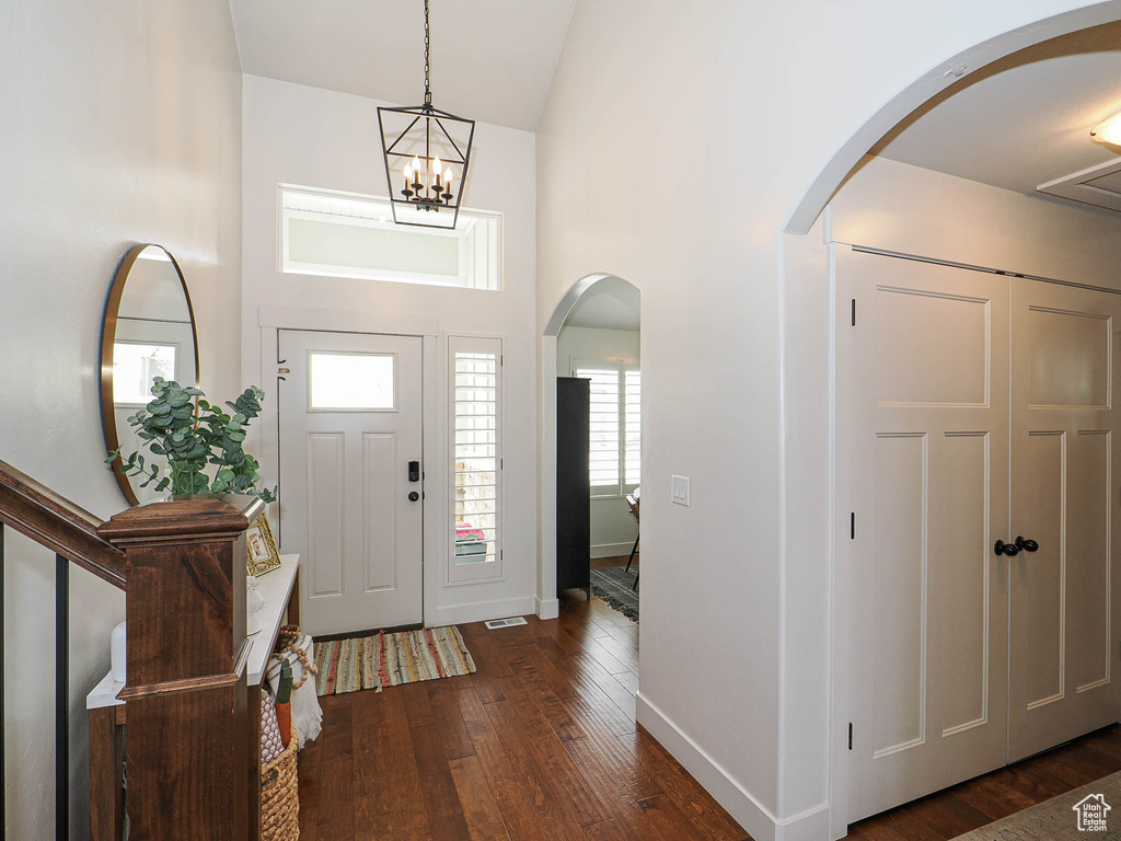 Foyer entrance with dark wood finished floors, a high ceiling, arched walkways, baseboards, and a chandelier