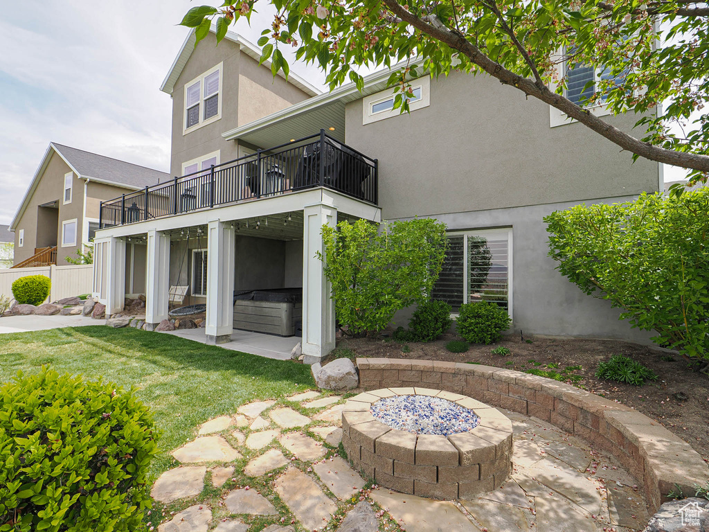 Rear view of house featuring a balcony, stucco siding, a patio, a lawn, and a fire pit