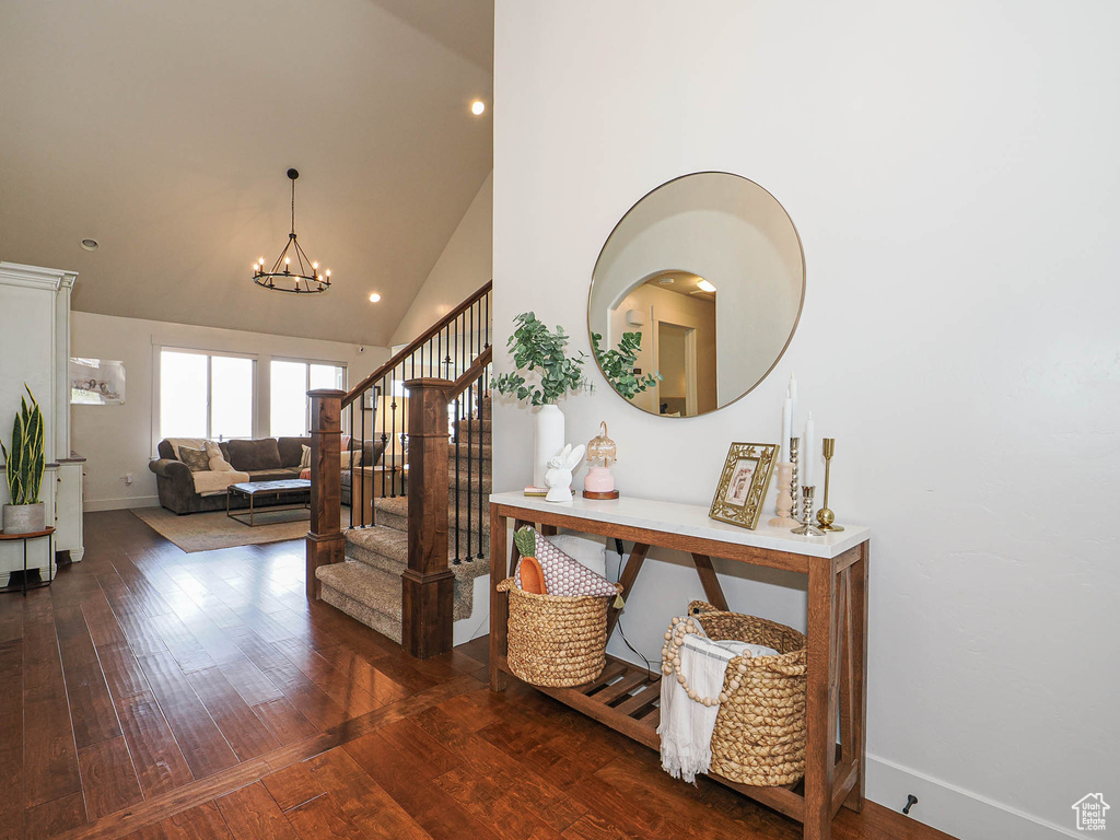 Corridor featuring high vaulted ceiling, wood-type flooring, baseboards, and a notable chandelier