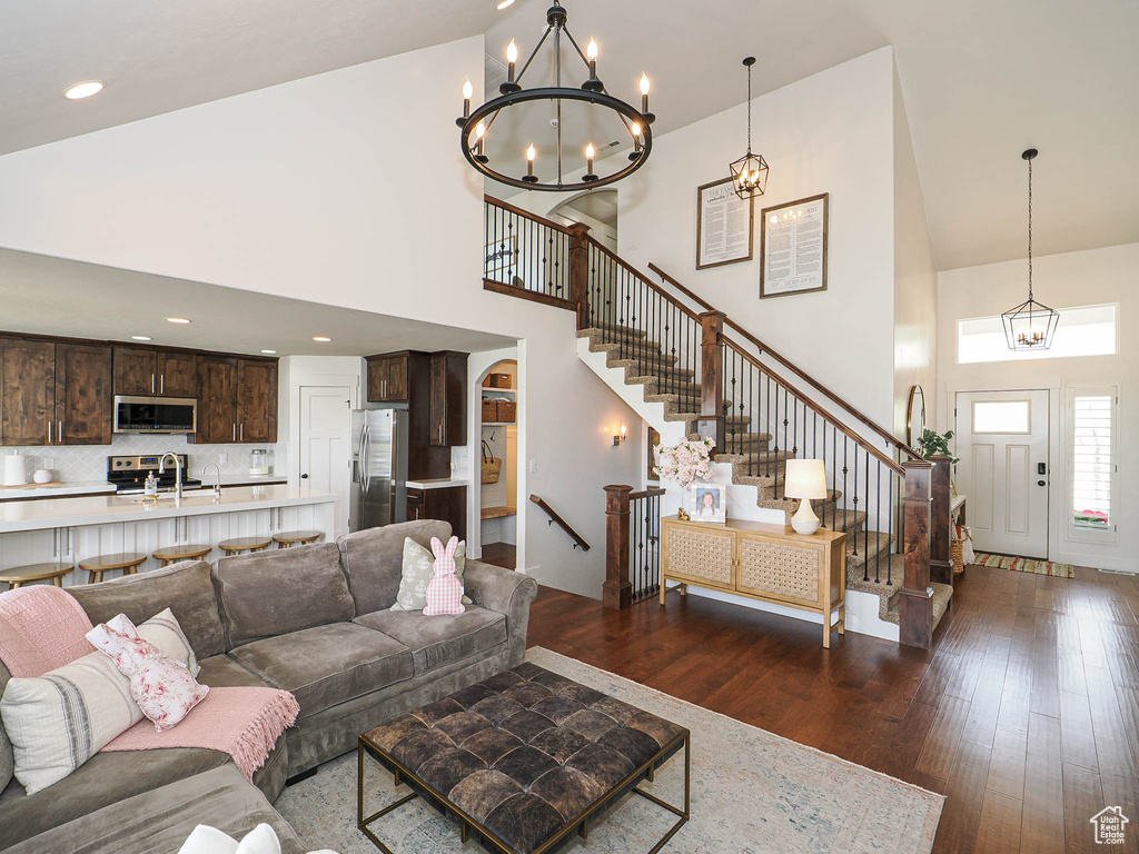 Living area with arched walkways, an inviting chandelier, stairs, high vaulted ceiling, and dark wood-type flooring